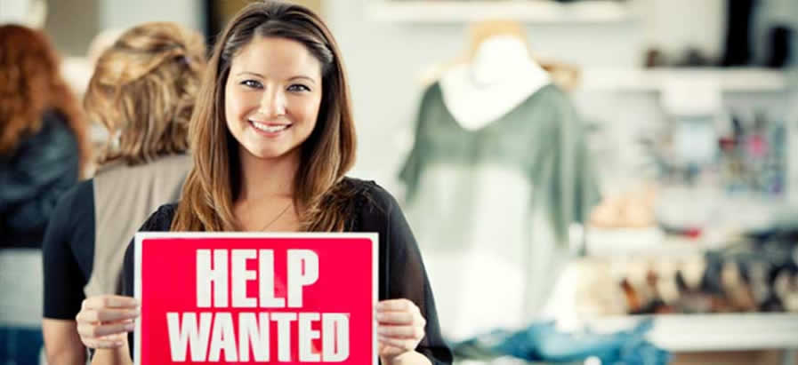 Woman business owner holding up help wanted sign.