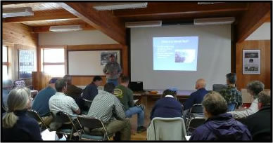 People sitting listening to a man presenting a slideshow in the front of the room.