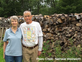 A couple standing by their stack of firewood.