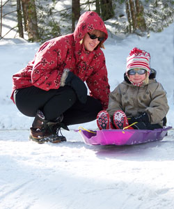 Mother helping toddler getting ready to slide in a pink plastic sled.