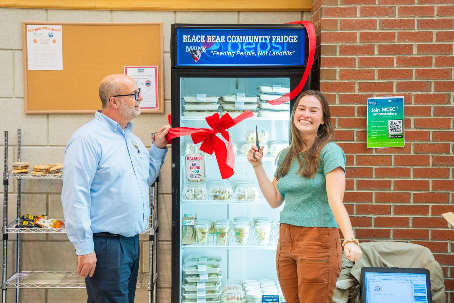 Kate Flynn cuts a red ribbon on a new community fridge at the University of Maine Orono.