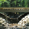 Side view of wooden bridge over small stream with streambed intacted.