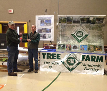 John Starrett and Harvey Chesley, with Pine Tree Camp's Outstanding Tree Farmer of the Year plaque, stand by the Maine Tree Farm display