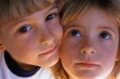 Young brother and sister with pressed cheeks, smiling.