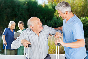 Caretaker helping older gentleman with crutches to stand.