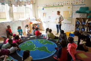 Elementary teacher standing in front of students seat on floor