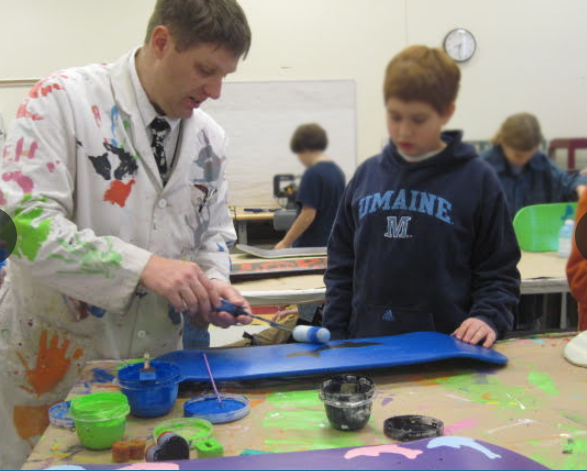 Mr. Kelley painting skateboard with student