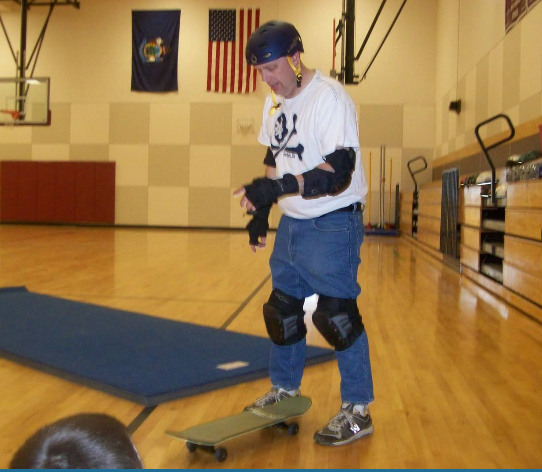 Mr. Kelley Skateboarding in Gym in Helmet and Pads