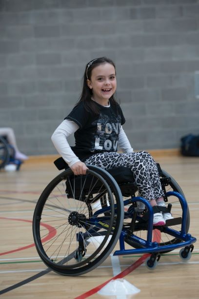 Young school aged girl sitting in a wheelchair in a school gymnasium