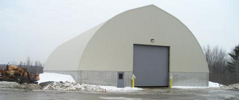 image of the sand and salt building with snow and parked construction equipment parked nearby