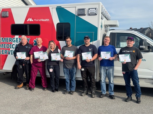 MaineHealth-Stephens Phoenix Award recipients standing and holding awards in front of an ambulance