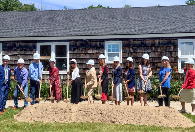 Line of people in white hardhats holding shovels filled with dirt