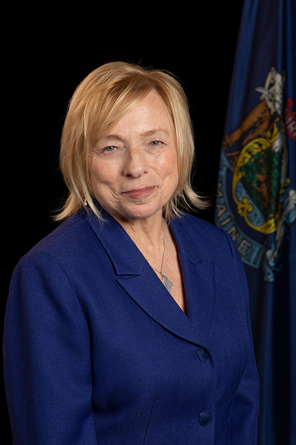 Governor Mills standing in front of the Maine State flag