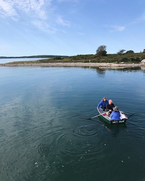 Three people rowing to shore in a dingy.