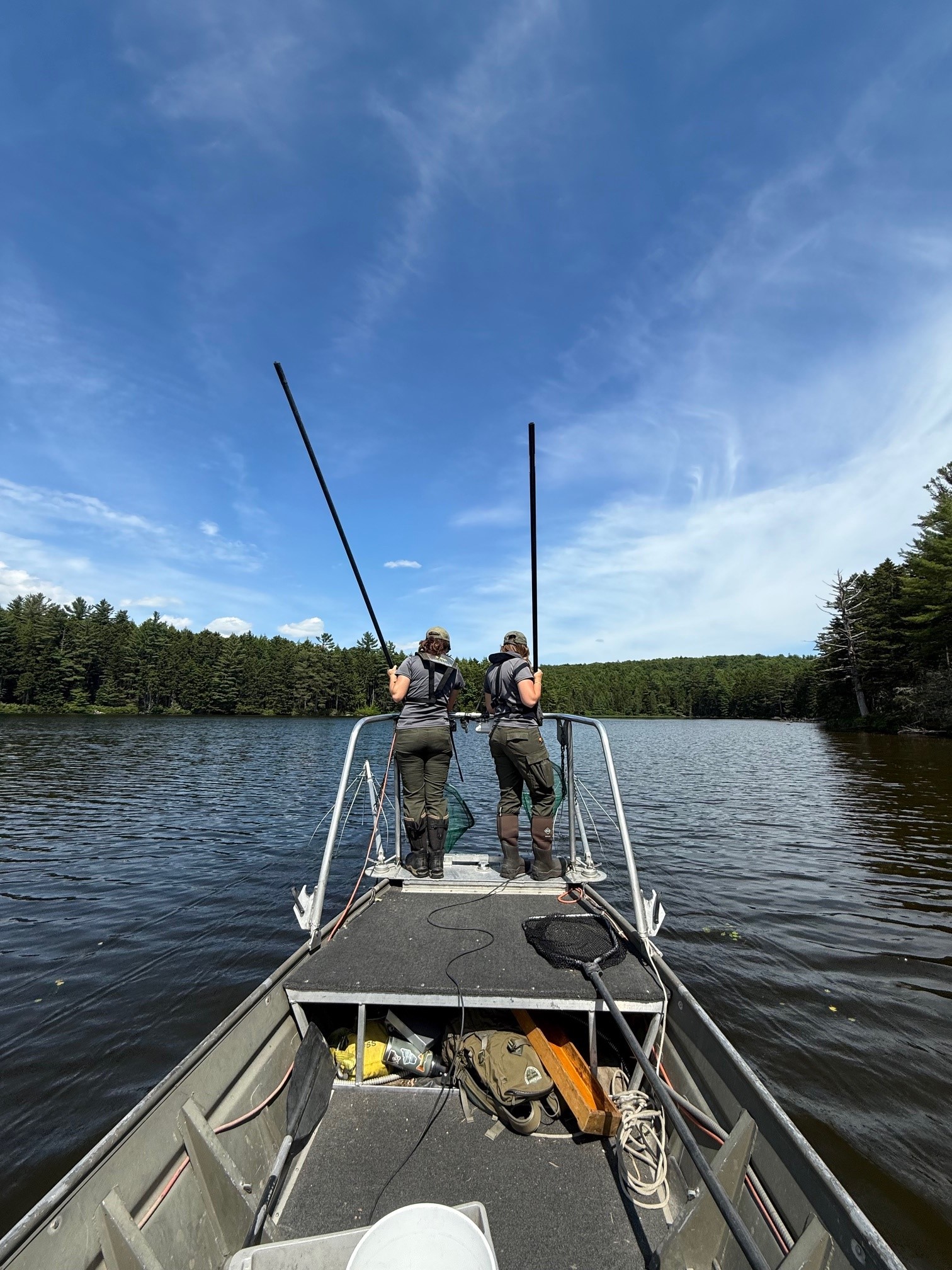 Two fisheries biologists standing on front of electrofishing boat on a undeveloped lake with blue skies