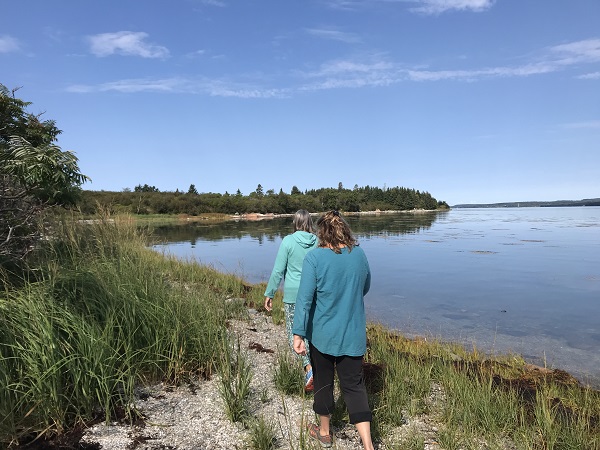 Two women walking the shoreline of an island at high tide.