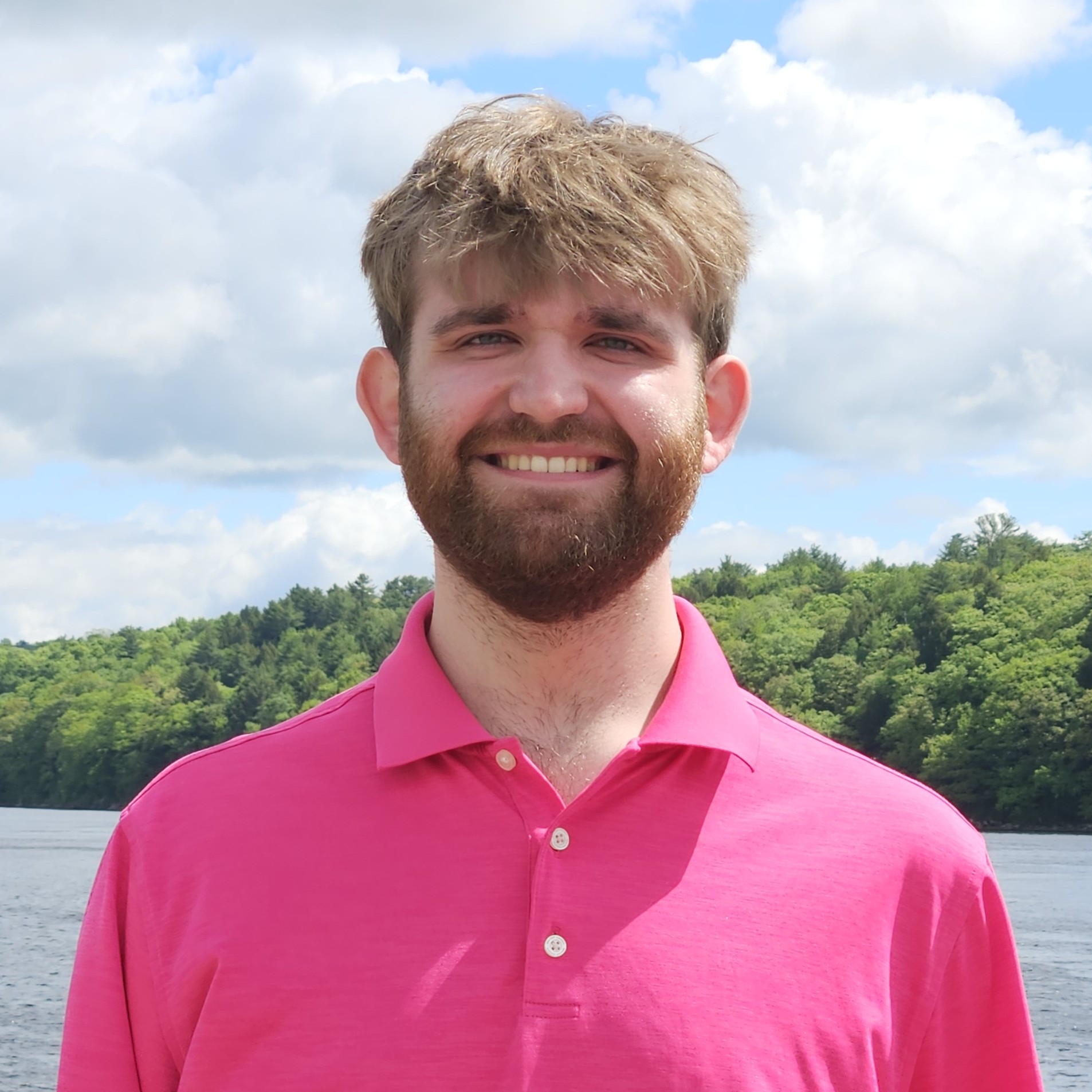 Kaiden in a pink shirt in front of a river on a sunny day.