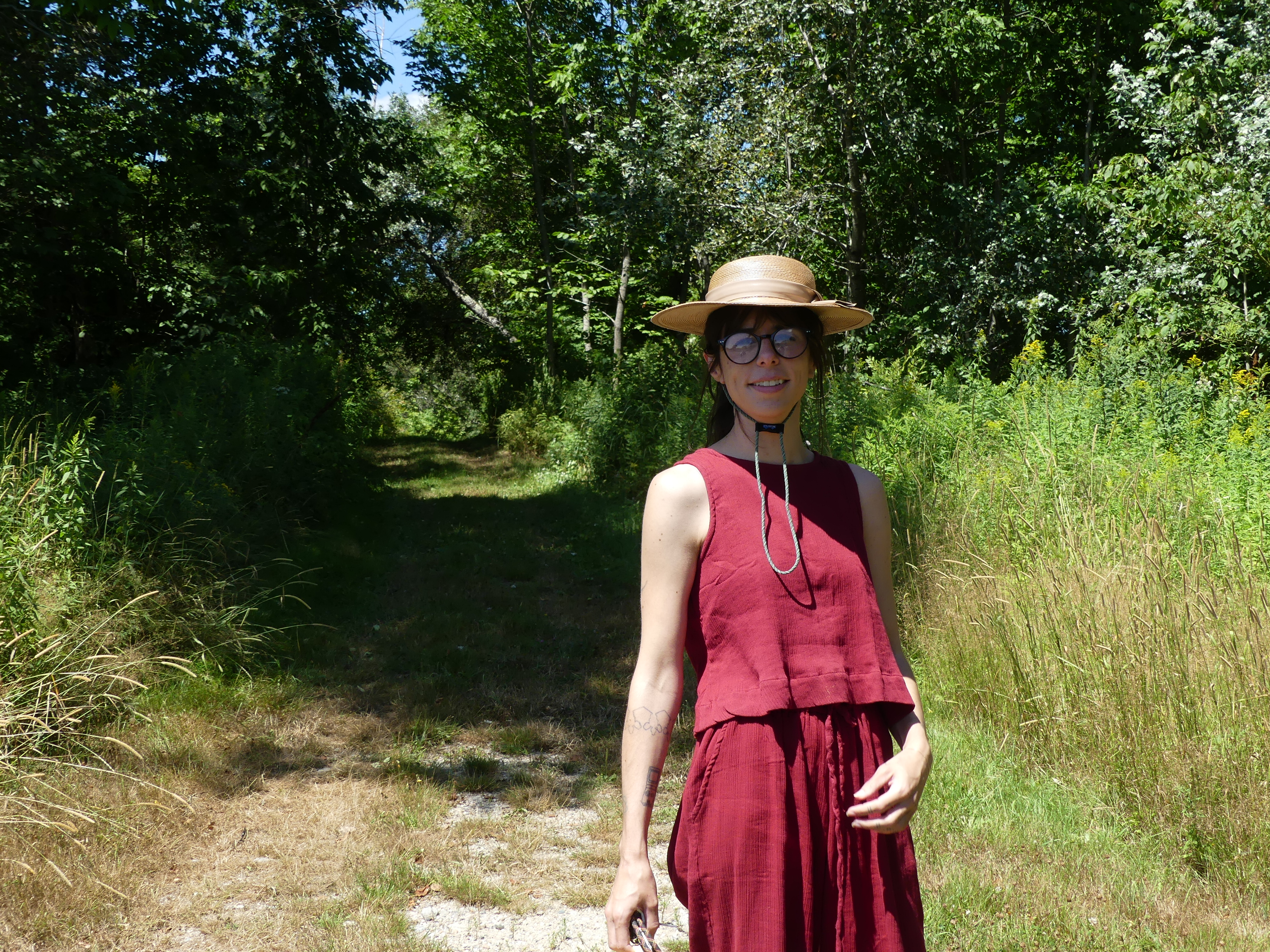 A woman wearing a straw hat, glasses, and red dress on a grassy path.