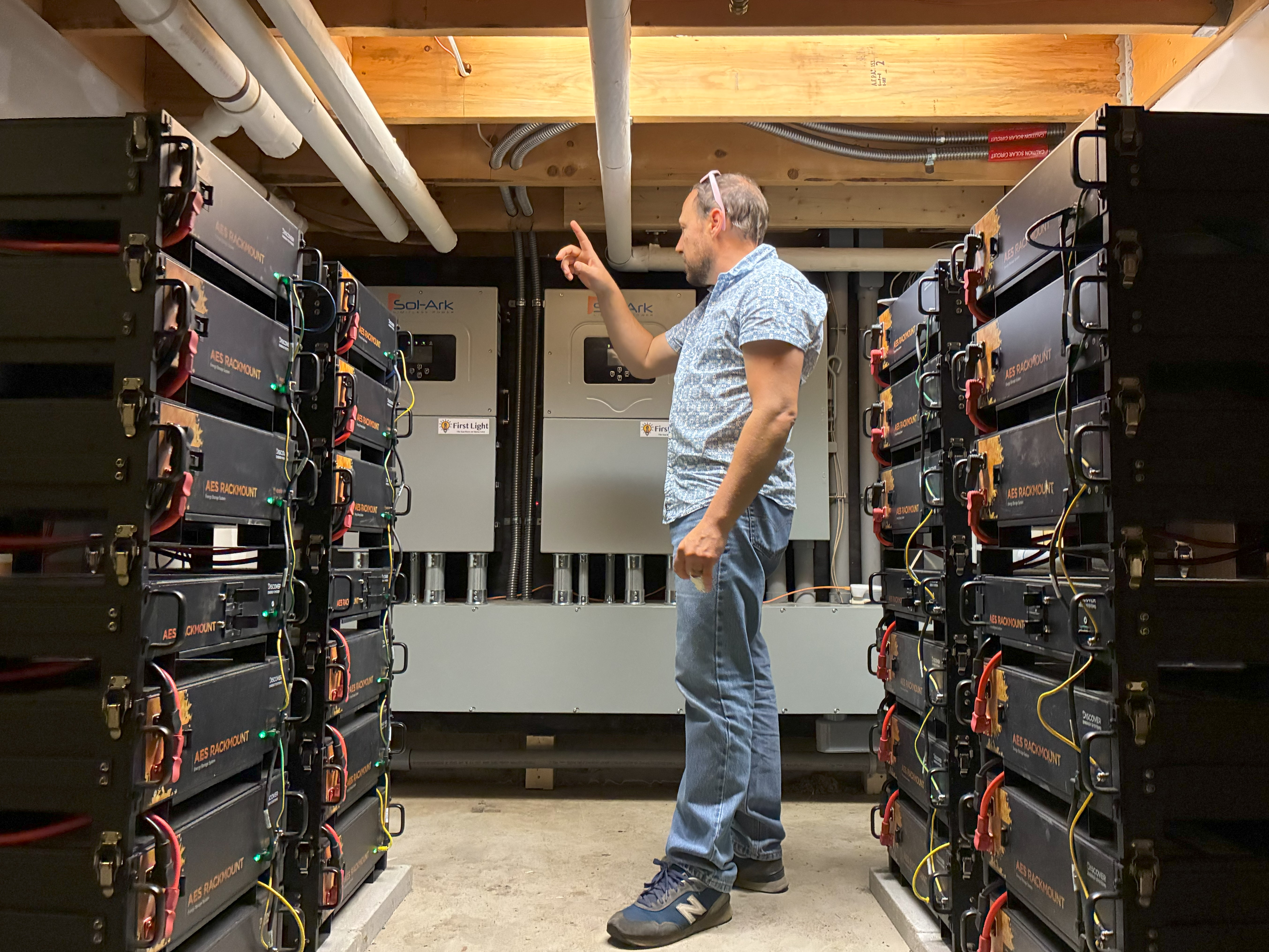 A man pointing to racks of batteries in a low ceilinged room.
