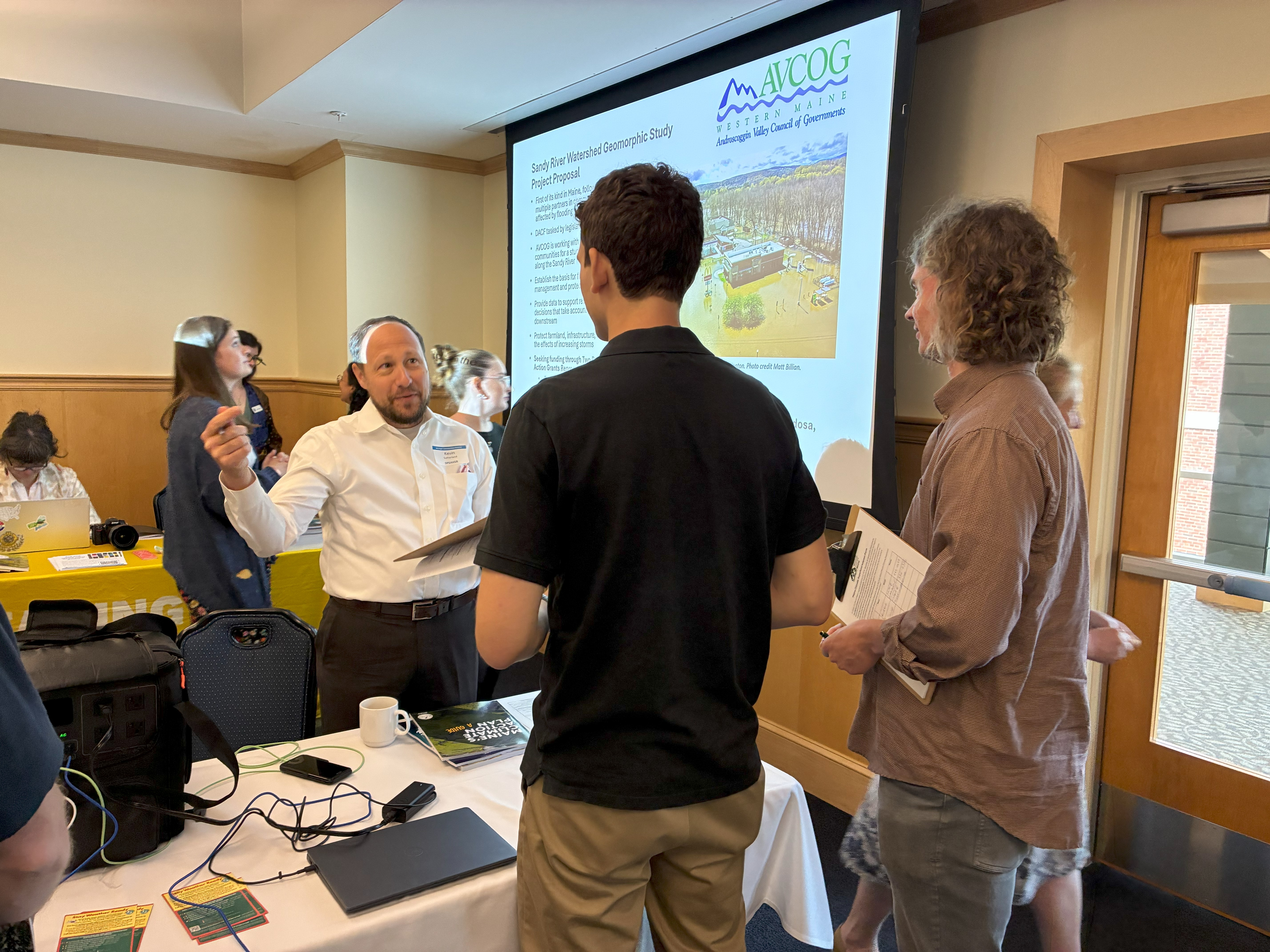 A man at a table at a conference talking to two people.