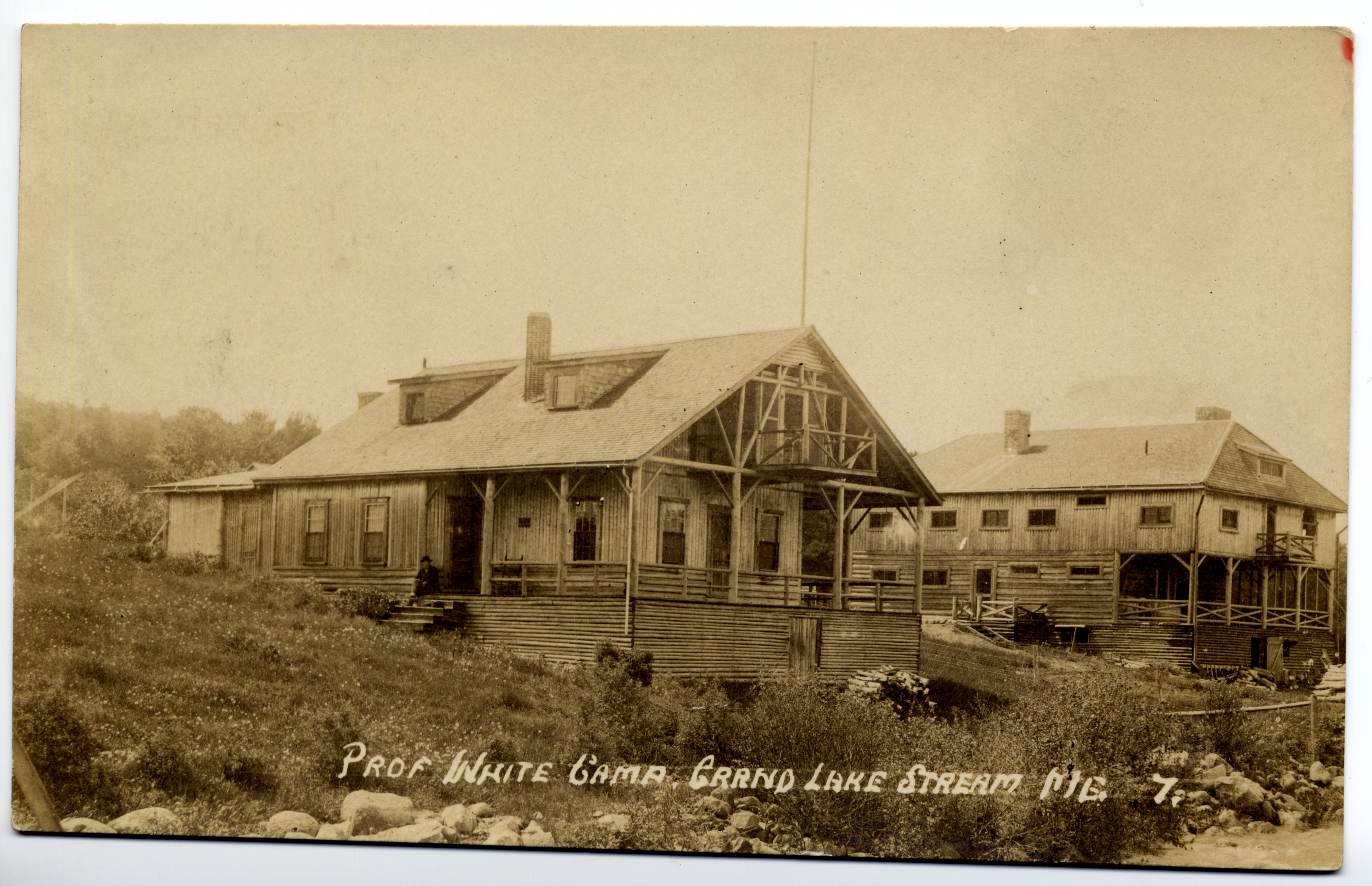 A black and white photograph of a large wooden sporting camp building with a wraparound porch at Grand Lake Stream, Maine, labeled "Prof White Camp."