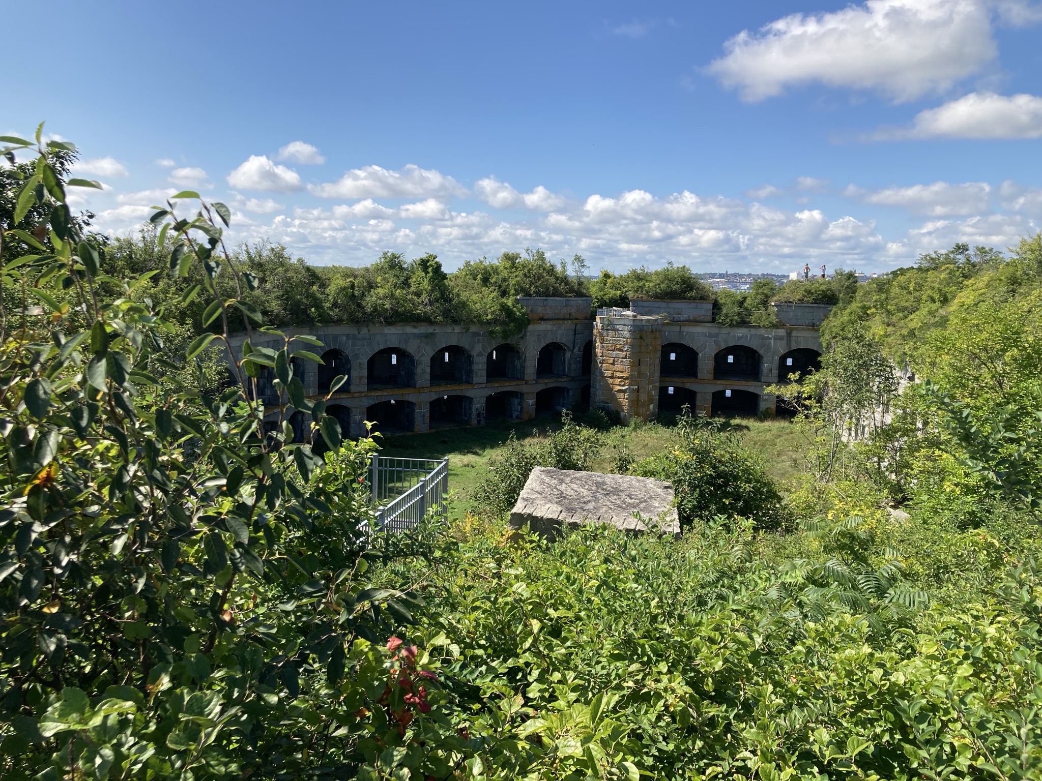 An elevated view looking down into the grassy interior courtyard of a semi-circular stone fort with rows of arched open bays, surrounded by thick green foliage.