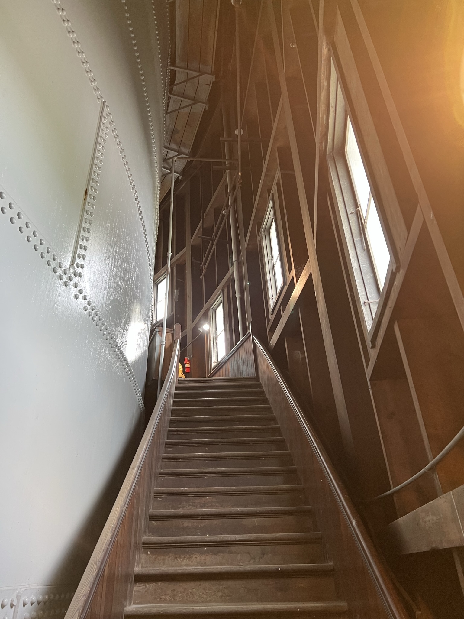 Interior view looking up the steep wooden staircase inside the Bangor Standpipe, with the riveted steel water tank visible on the left and dark timber framing on the right.