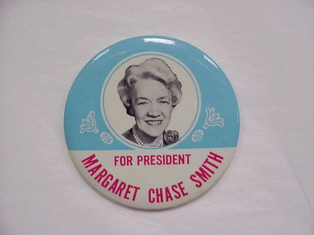 "Round campaign button with a black-and-white portrait of a smiling woman with short curled hair and pearl necklace, reading 'For President, Margaret Chase Smith' on a light blue and white background."
