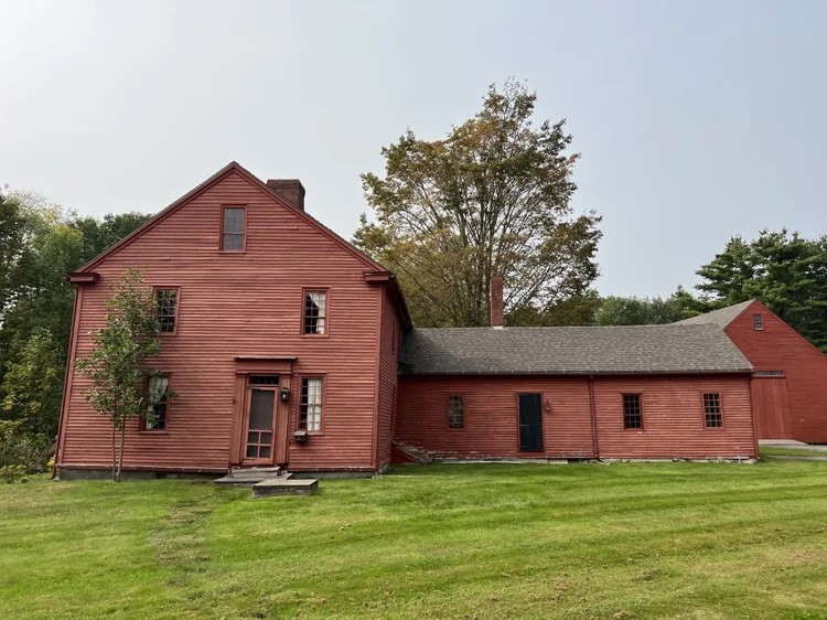 Red-painted historic wood-frame house with an attached one-story wing and grassy lawn, viewed from the front.
