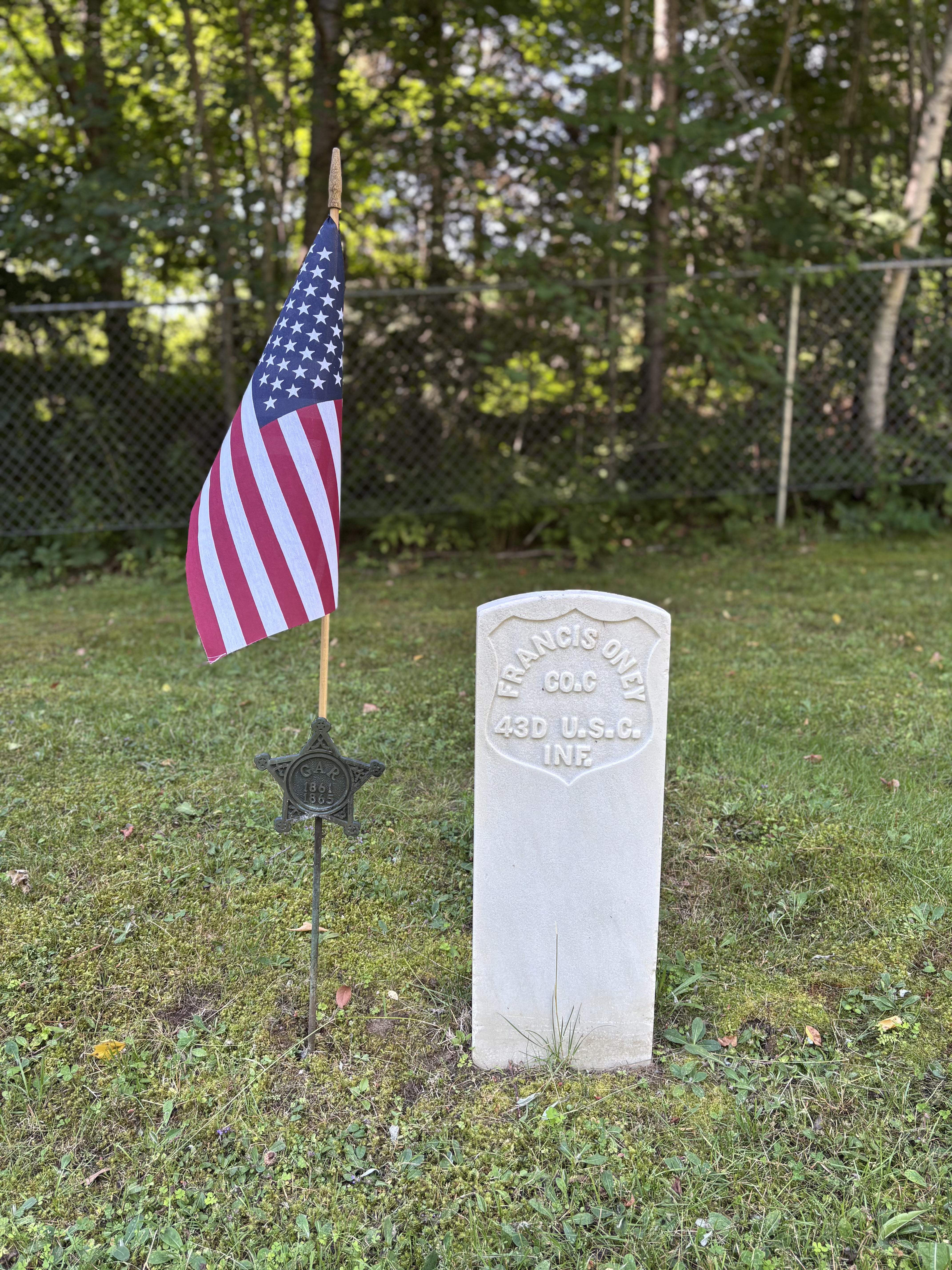A military headstone for Francis Oney of the 43rd U.S. Colored Infantry, accompanied by an American flag and a GAR marker.