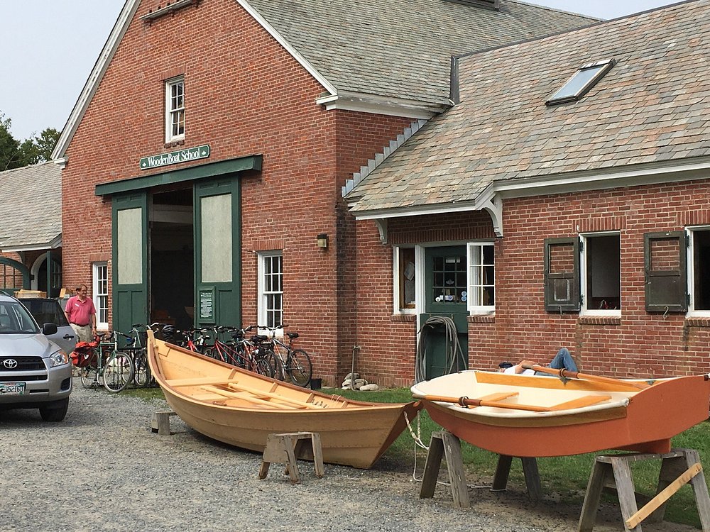 Exterior view of the brick WoodenBoat School building with two small wooden rowboats displayed on sawhorses in front.