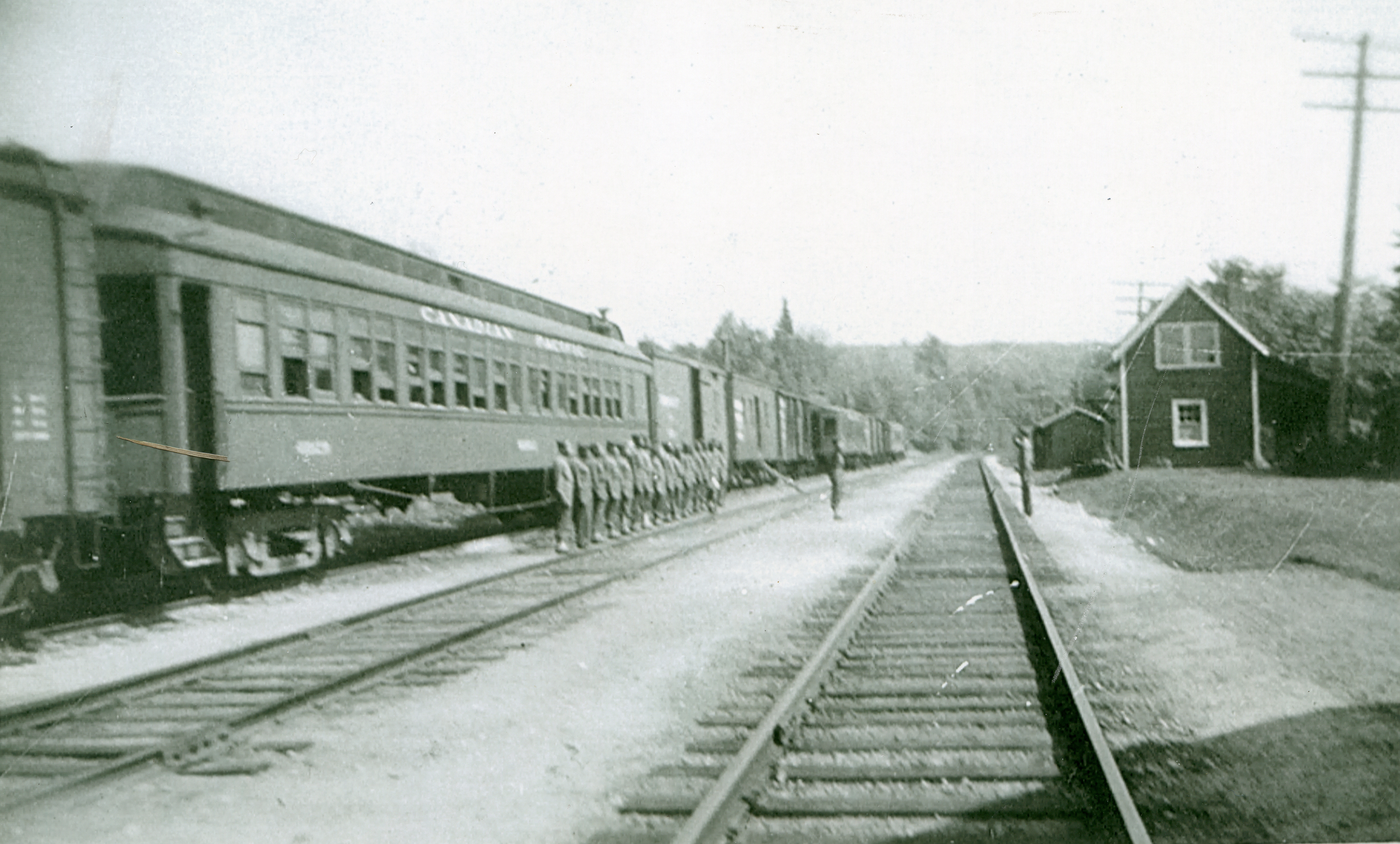 A black-and-white photo of a line of soldiers standing beside a Canadian Pacific train parked on railway tracks near a station.