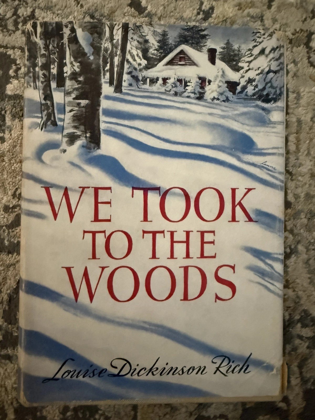 Vintage book cover of "We Took to the Woods" by Louise Dickinson Rich, showing a snow-covered cabin among birch and pine trees.