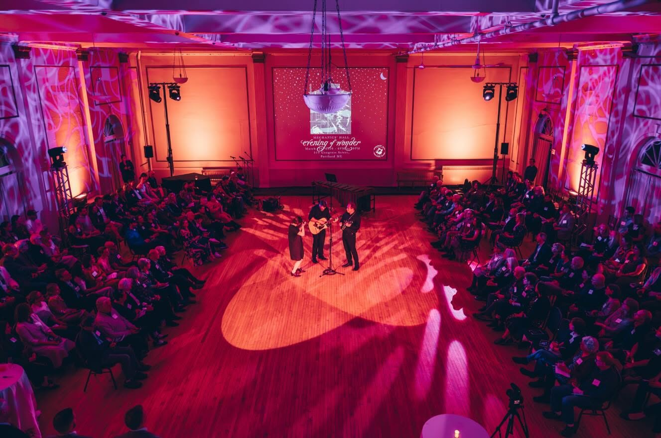 A wide-angle view of a grand ballroom lit in purple and pink tones, with two performers on a central wooden floor surrounded by a seated audience.