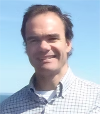 photo of a white mail in a button down shirt, smiling with blue sky behind him